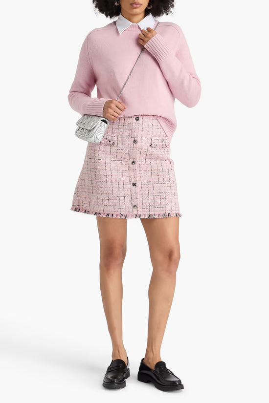 Woman wearing pink metallic tweed mini skirt with frayed hem, paired with pink sweater and black loafers — Maje | Endless UAE