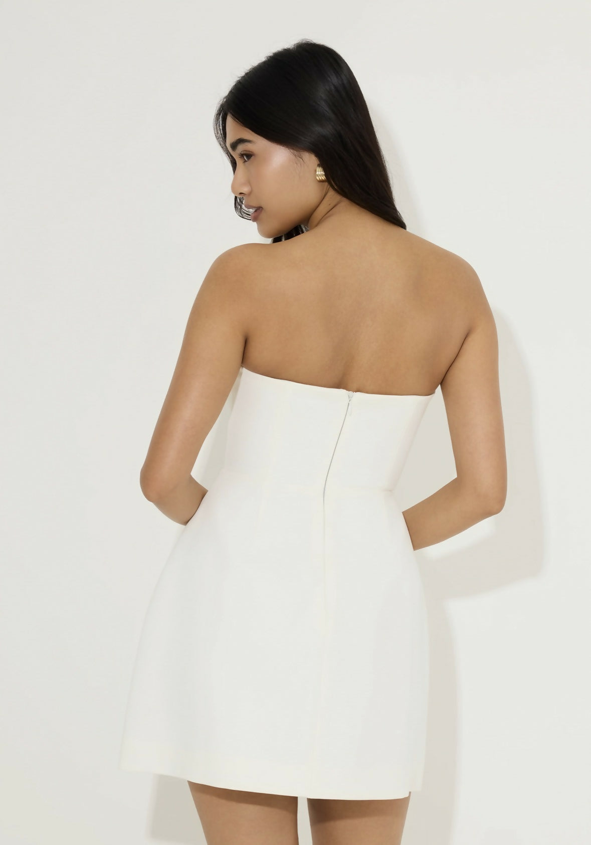 Woman wearing white strapless mini dress with back zipper closure, viewed from behind — Odd Muse | Endless UAE